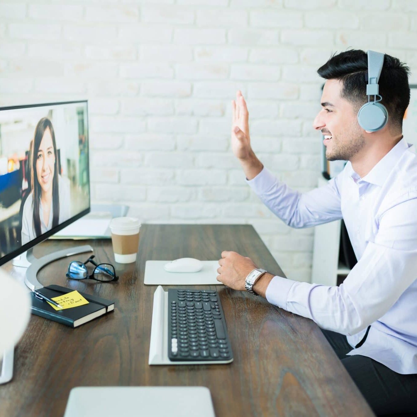 Professionals Greeting Through Conference Call Confident young salesman waving at colleague during video call on computer at desk